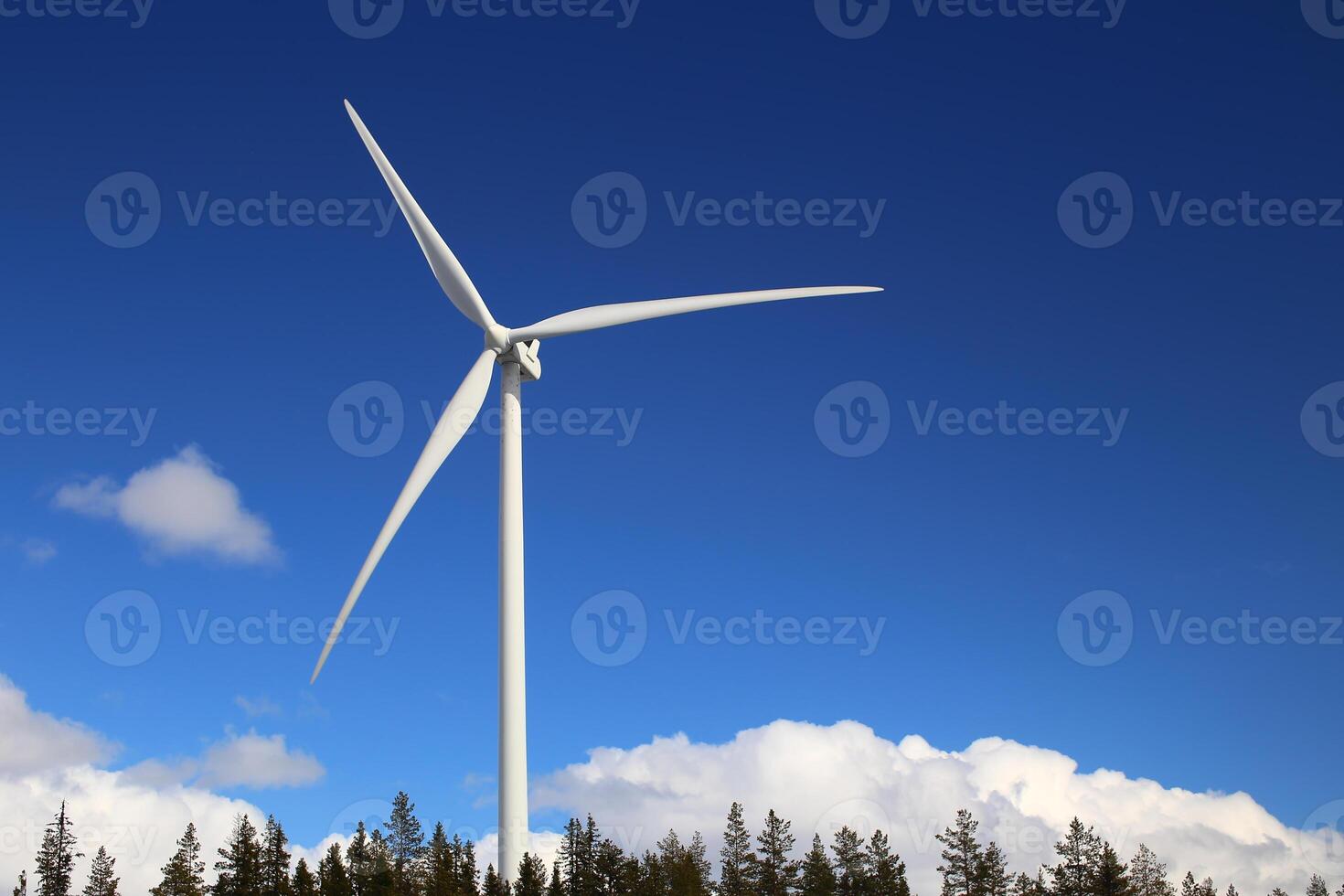 Wind turbine over forest and clouds with blue sky photo
