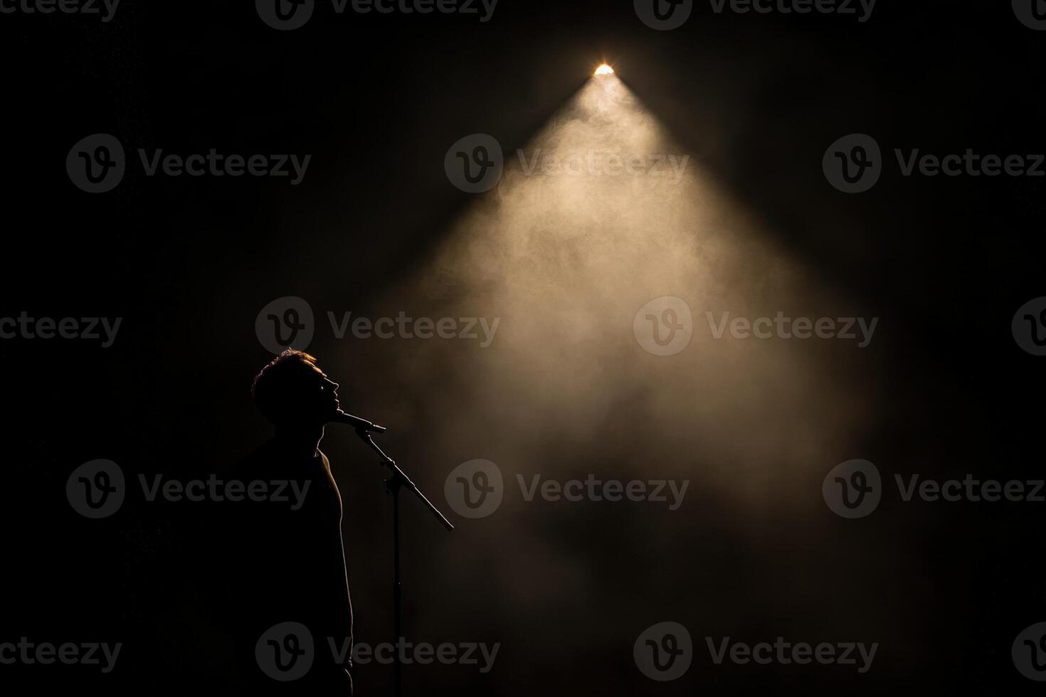 Silhouette of a man singing in front of a spotlight photo