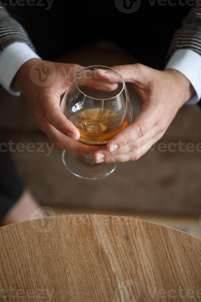 A man businessman holds a glass with alcohol in his hand. Dressed in a jacket and shirt. Rest after a working day photo