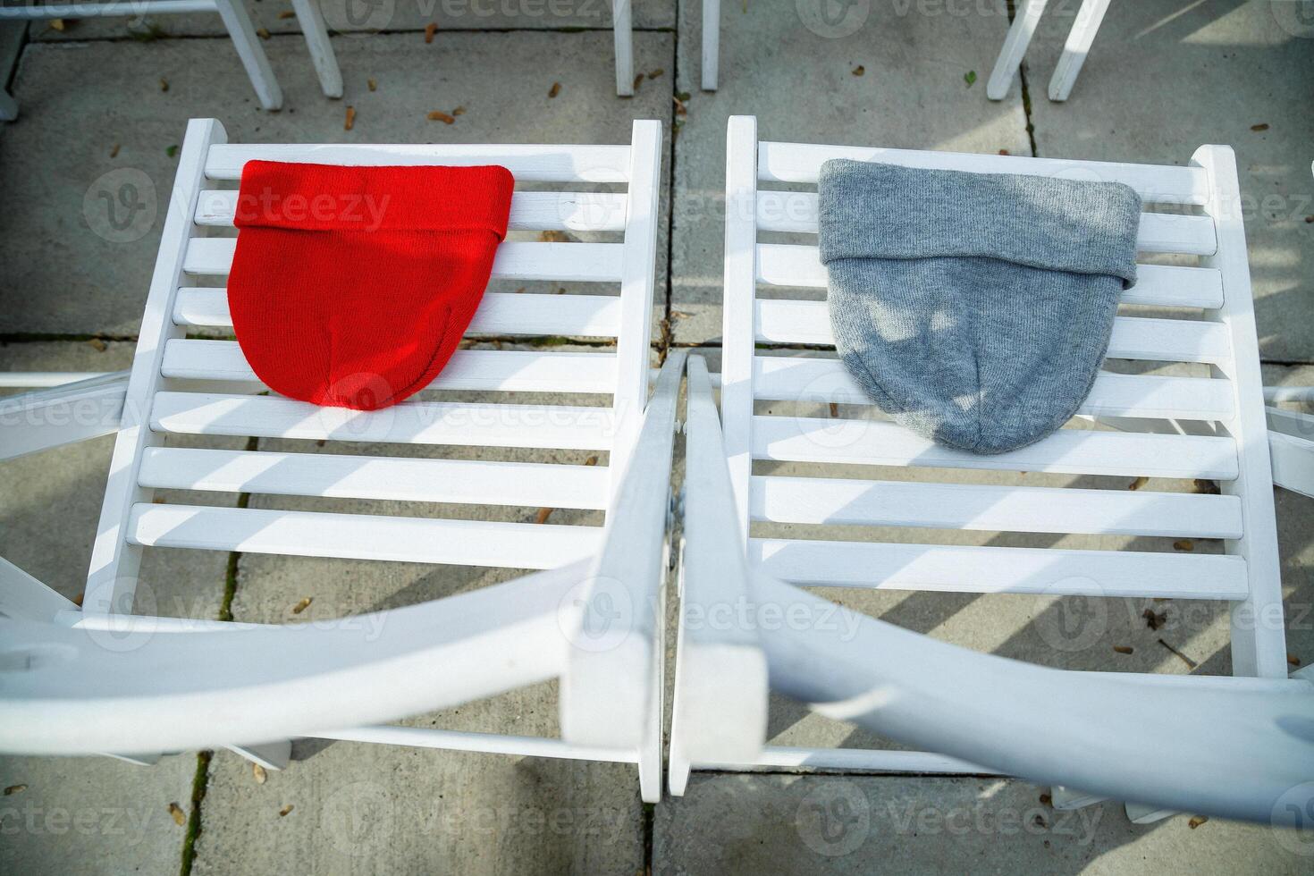 Two hats of red and gray on white chairs photo