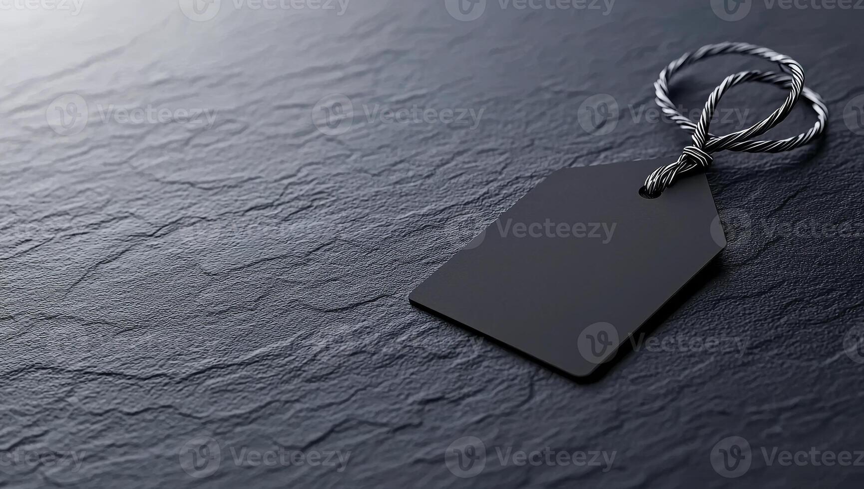 Simple black tag on textured surface for branding. A plain black tag rests on a dark textured surface, suitable for crafting, labeling, or branding purposes. photo