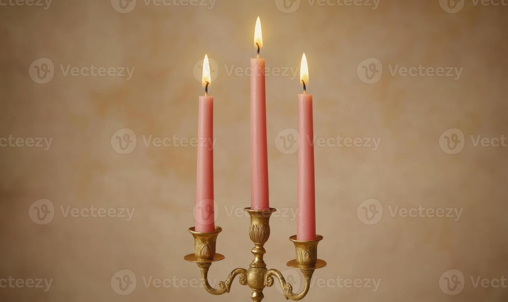 Three pink candles are lit and sitting on a gold candlestick photo