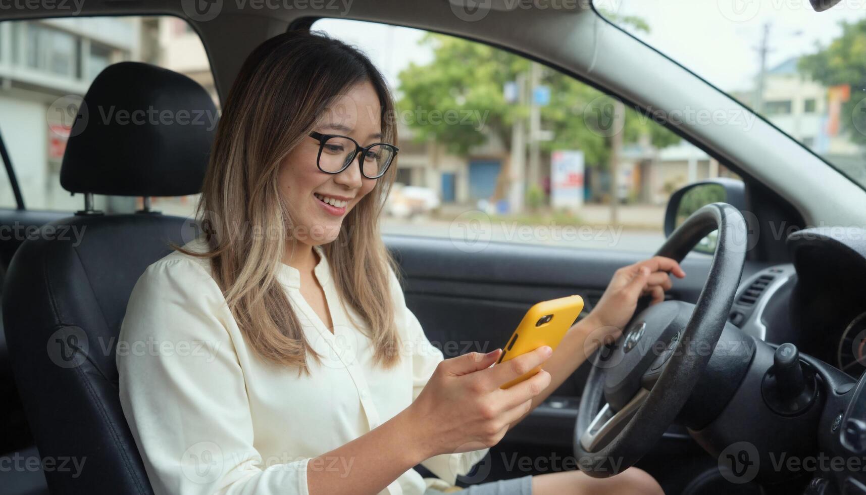 A woman with glasses and a yellow phone uses a car She's in a white shirt, smiling, in a city photo