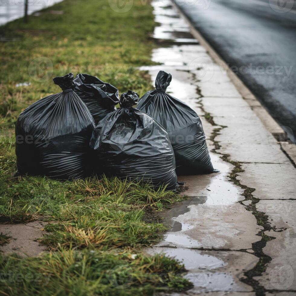 Black trash bags on wet grass beside cracked pavement, road in background For Social Media Post Size photo
