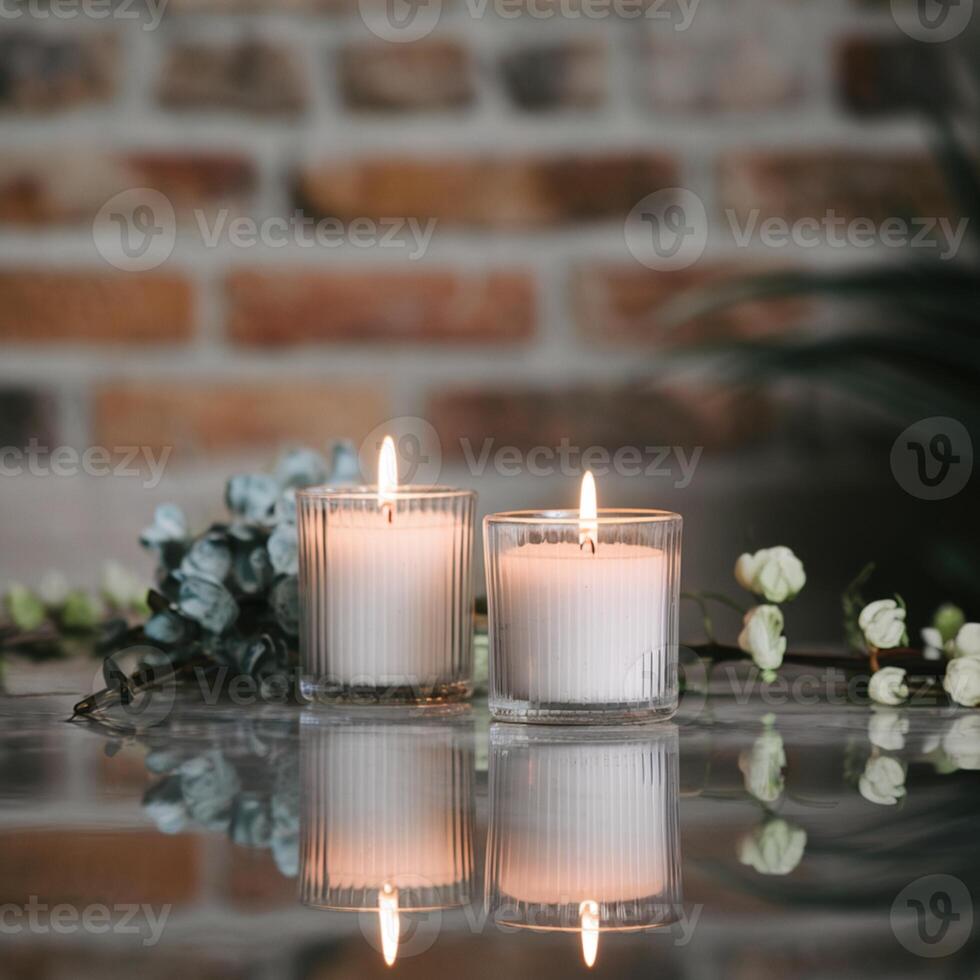 White candles in glass holders burn on reflective surface, blurred brick wall background For Social Media Post Size photo
