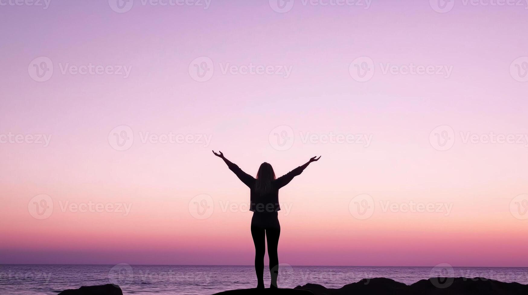 Woman raising outstretched arms to the pink sky at sunset over the ocean photo