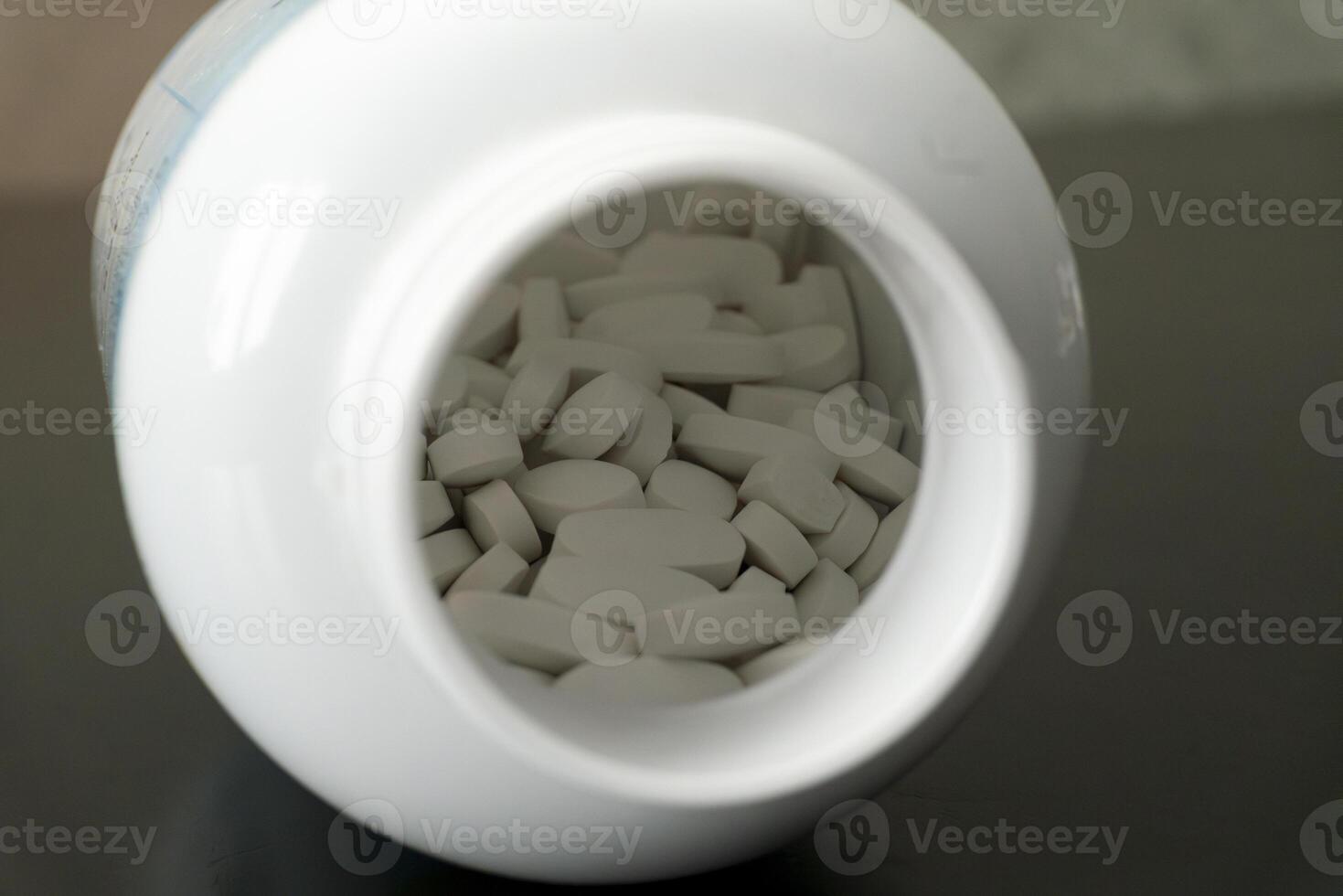 White tablets spilling out of a bottle on a dark surface photo