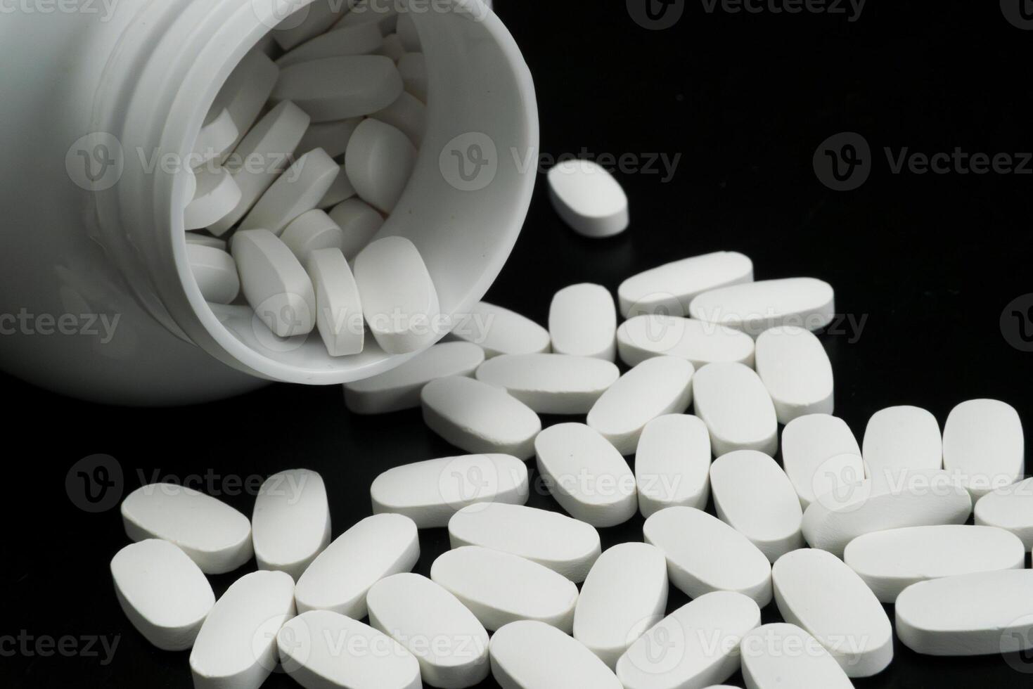 Pills spilling from a white bottle on black surface photo