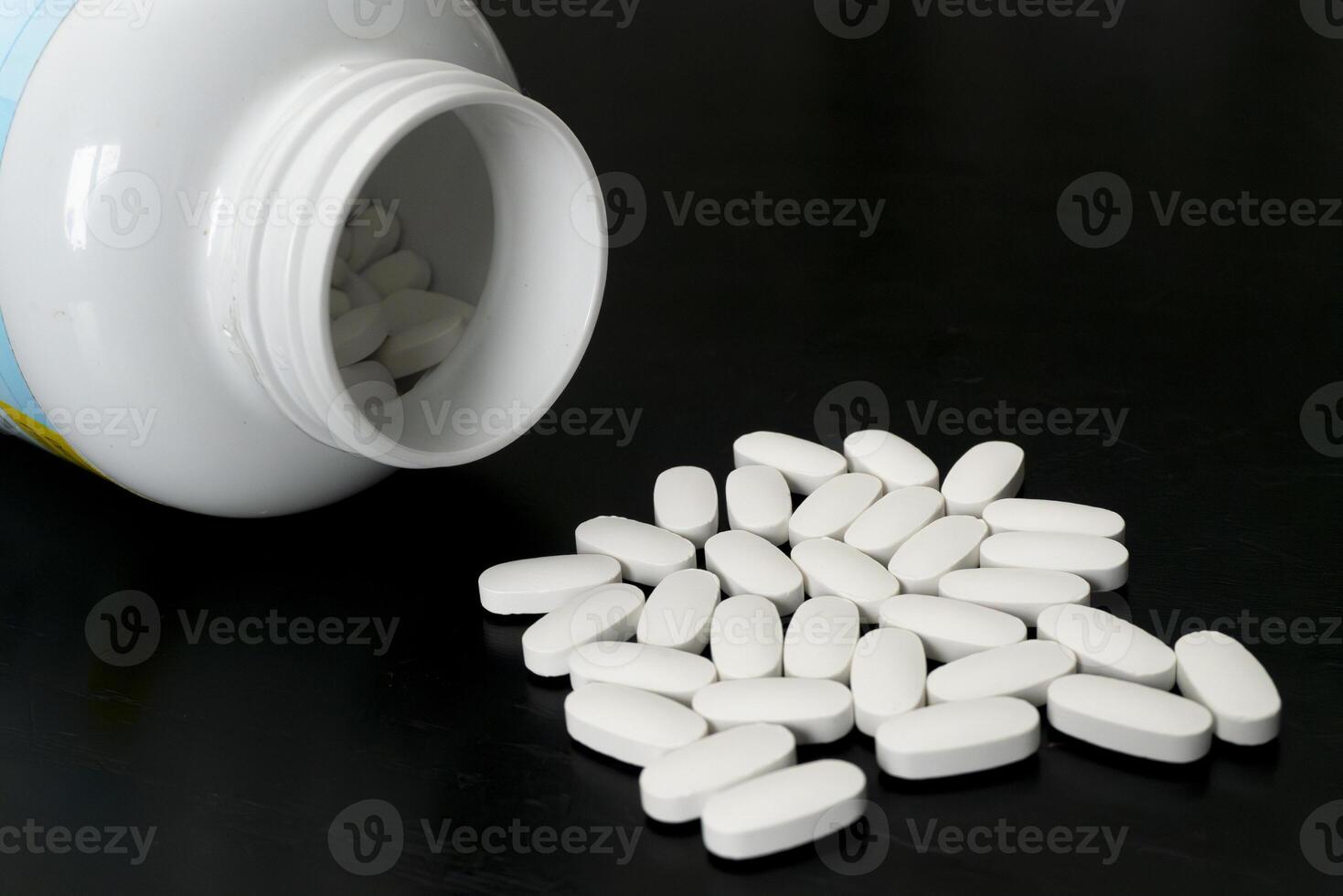 White tablets spilled from a bottle on a black surface photo