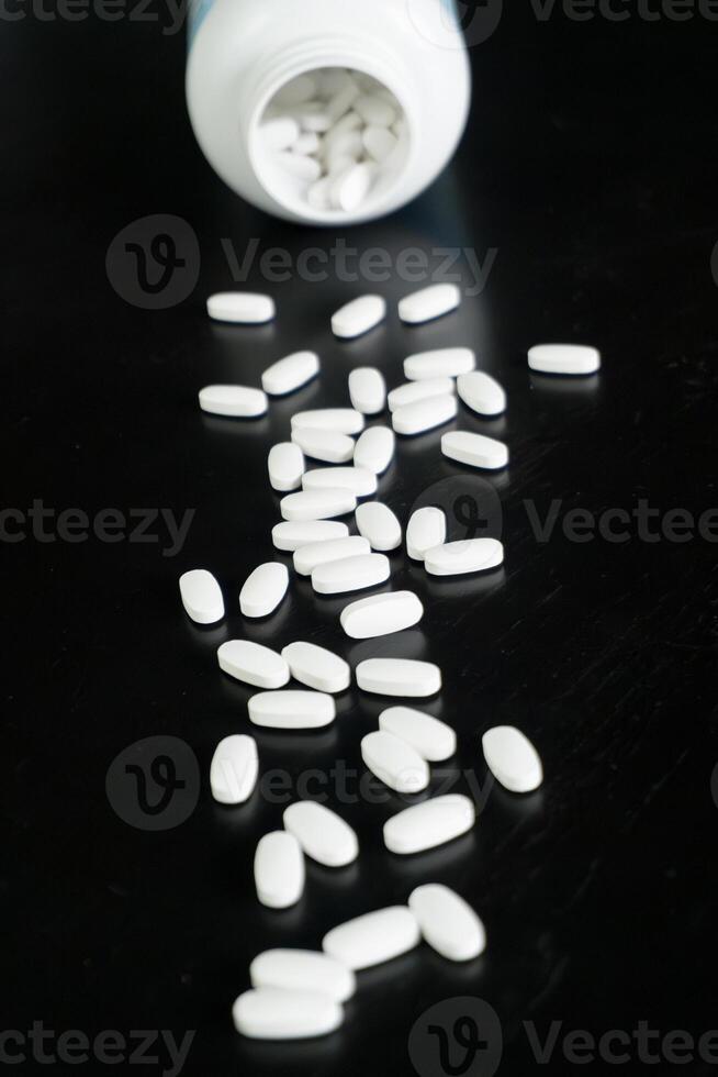 White tablets spilled from a bottle on a dark surface in a studio photo