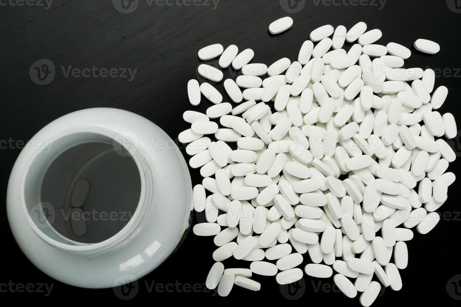 White tablets spilled from a container on dark surface photo