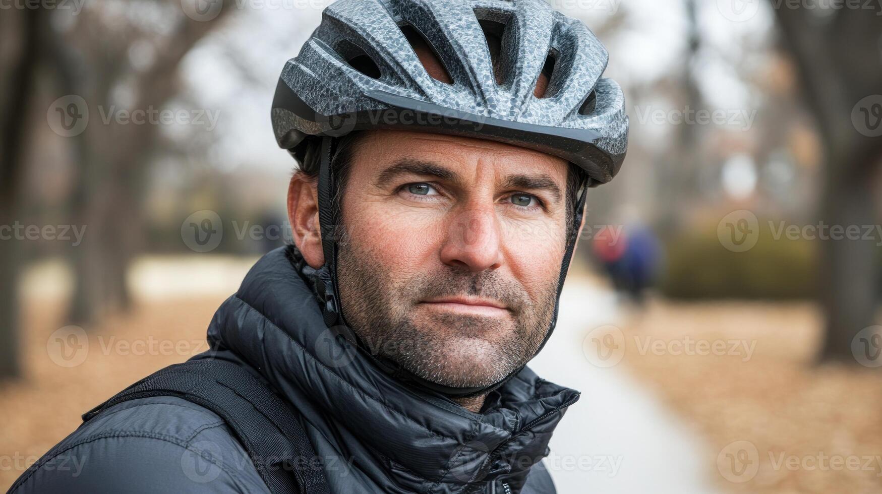 A man wearing a helmet and winter jacket pauses to enjoy the quiet beauty of a leaf-strewn park photo