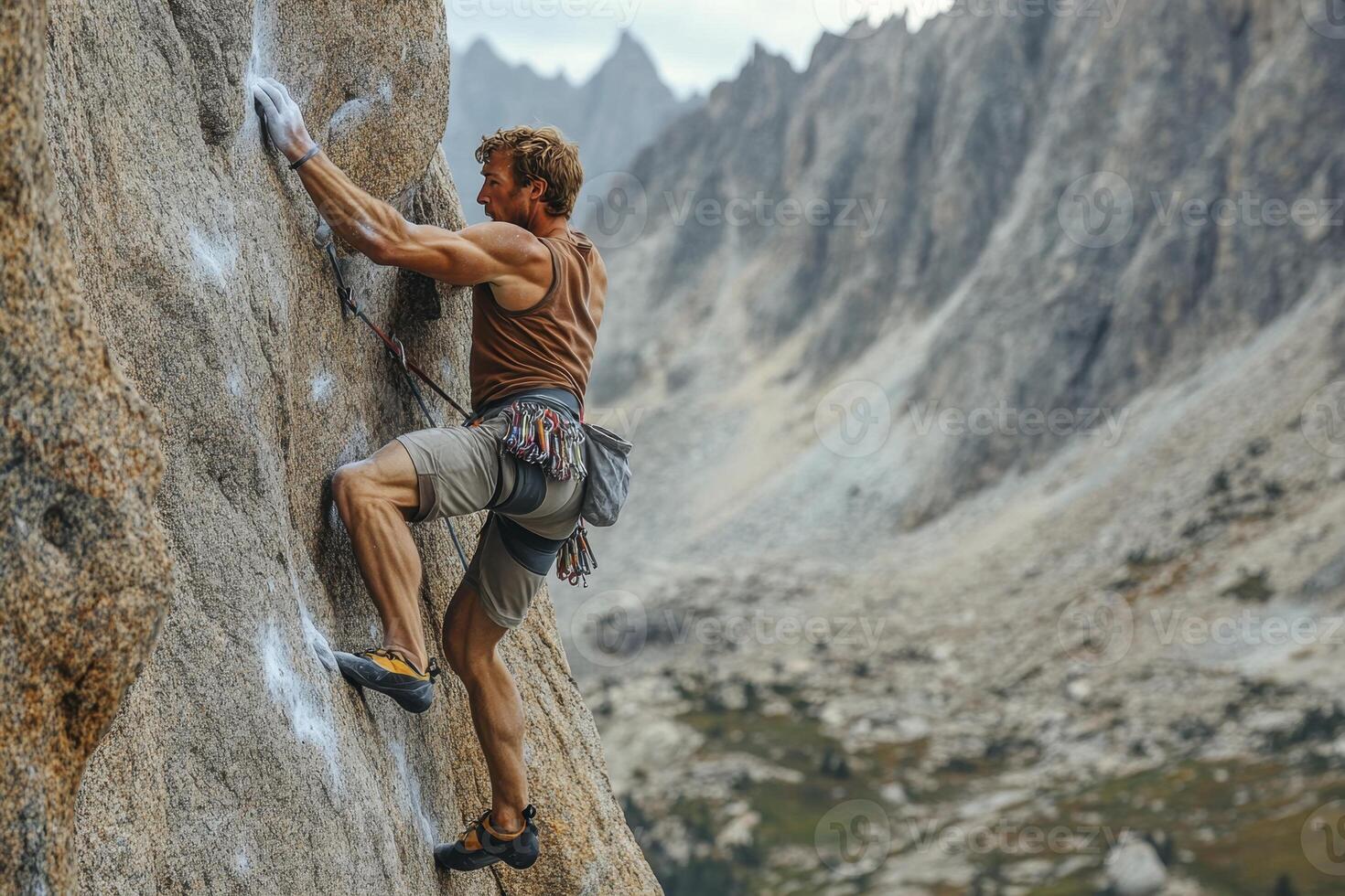 A muscular male climber ascends a steep rock face in a mountainous landscape photo