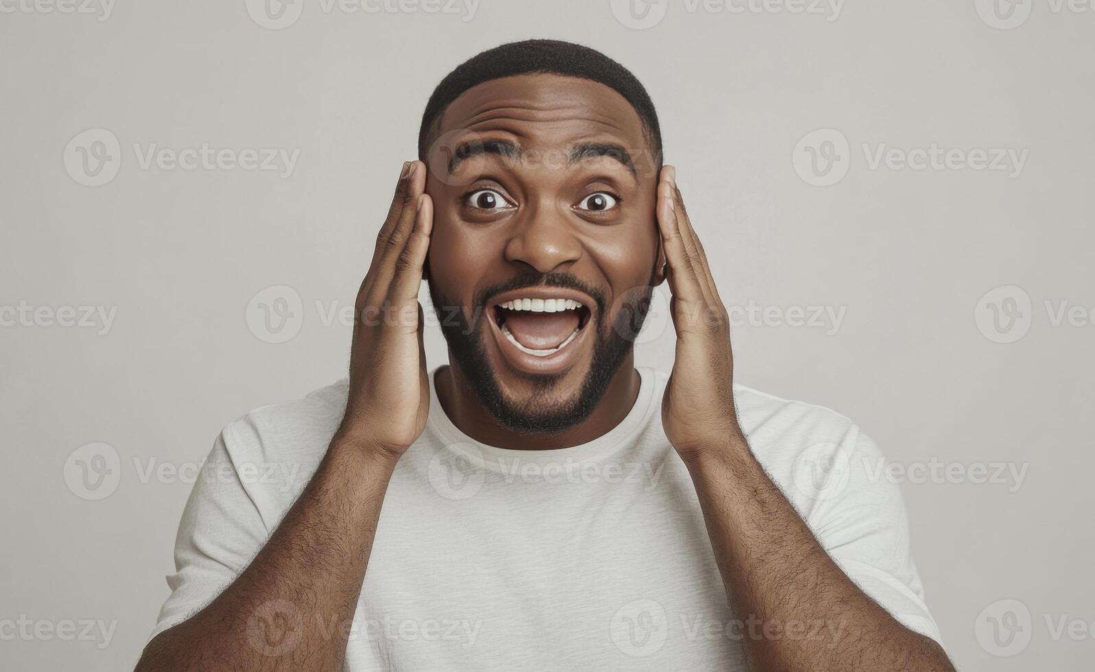 A portrait of a surprised young Black man with hands on his head, mouth open in a joyful, shocked expression against a neutral background photo