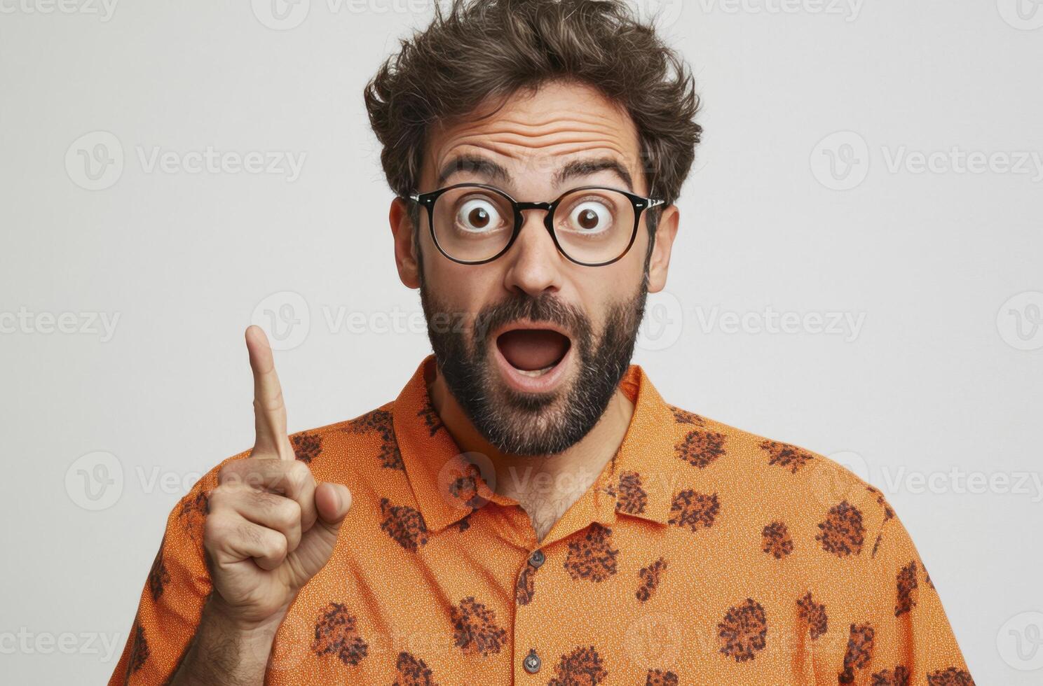 A man with surprised expression, wearing glasses and an orange shirt, points upward with one finger, suggesting an idea or epiphany. Studio shot on light background. photo
