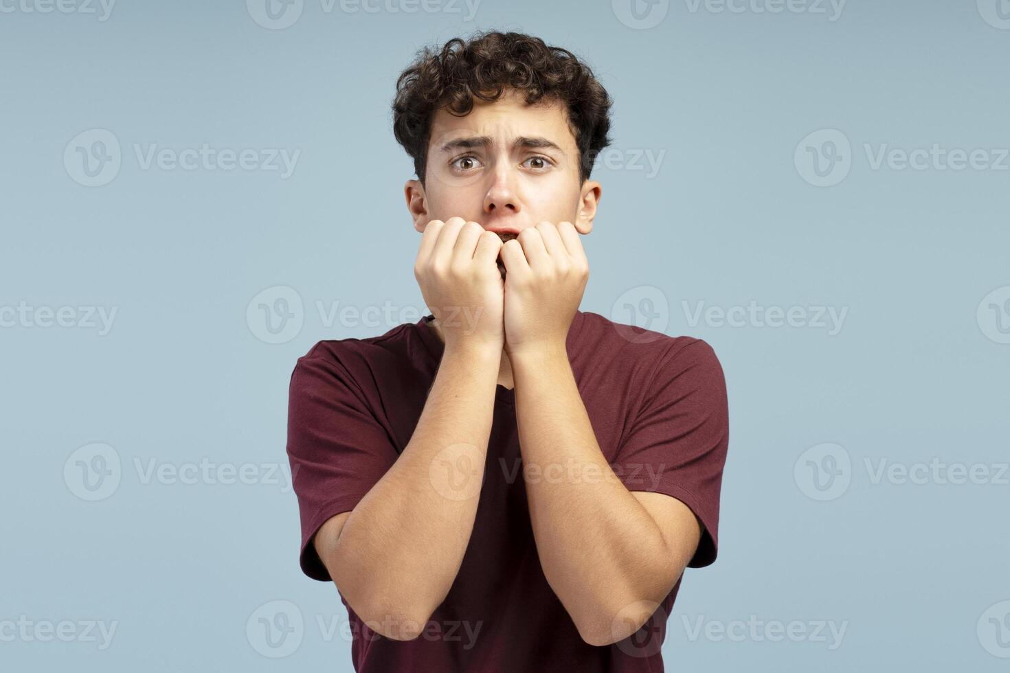 Scared shocked boy, pupil wearing red t shirt looking at camera standing isolated on blue background photo