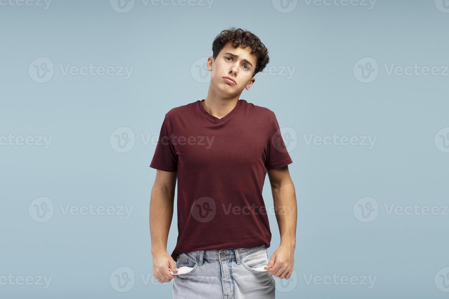 Upset teen boy wearing casual clothes showing empty pockets, standing isolated on blue background photo