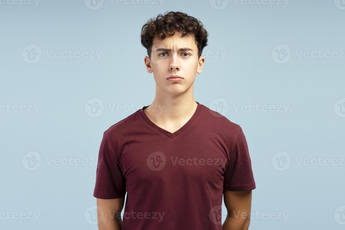 Portrait of serious, pensive, sad young teen boy wearing red t shirt, looking at camera photo