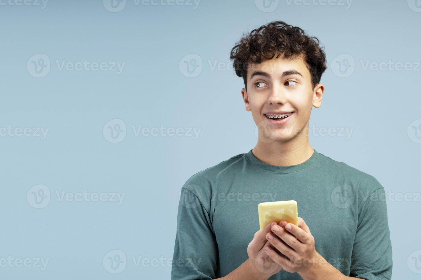 Happy boy wearing green t shirt, holding mobile phone, using mobile app, looking away on copy space photo