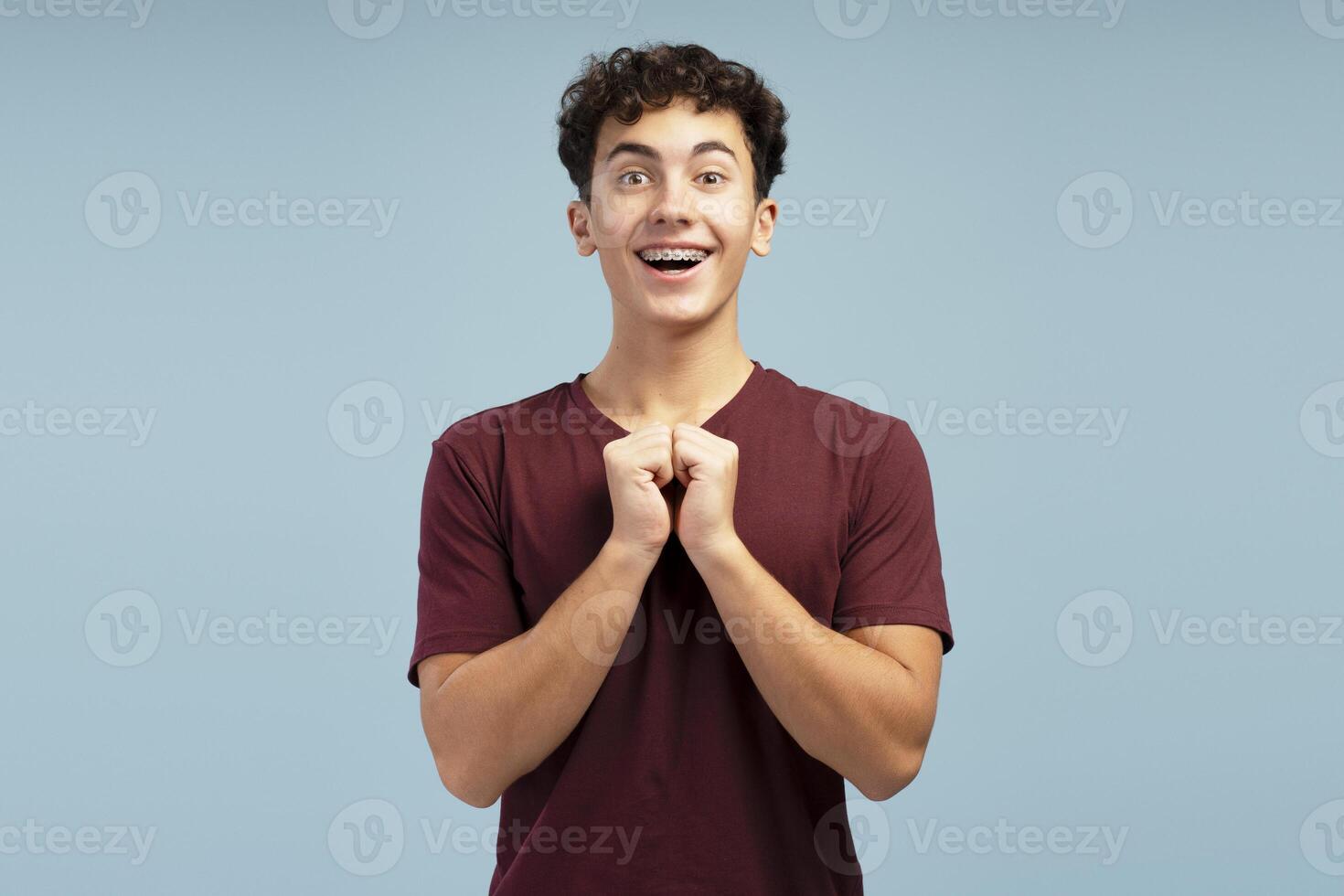 Portrait of excited teen boy with braces looking at camera standing isolated on blue background photo