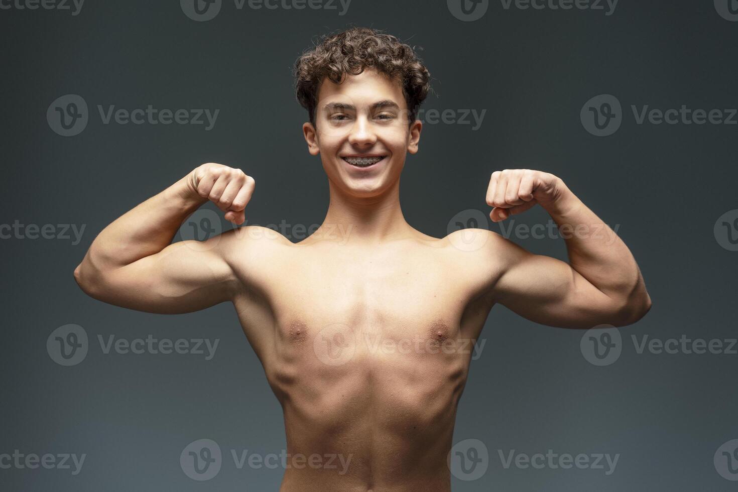 Portrait of smiling, happy, attractive teenager boy with naked torso showing muscles hands photo