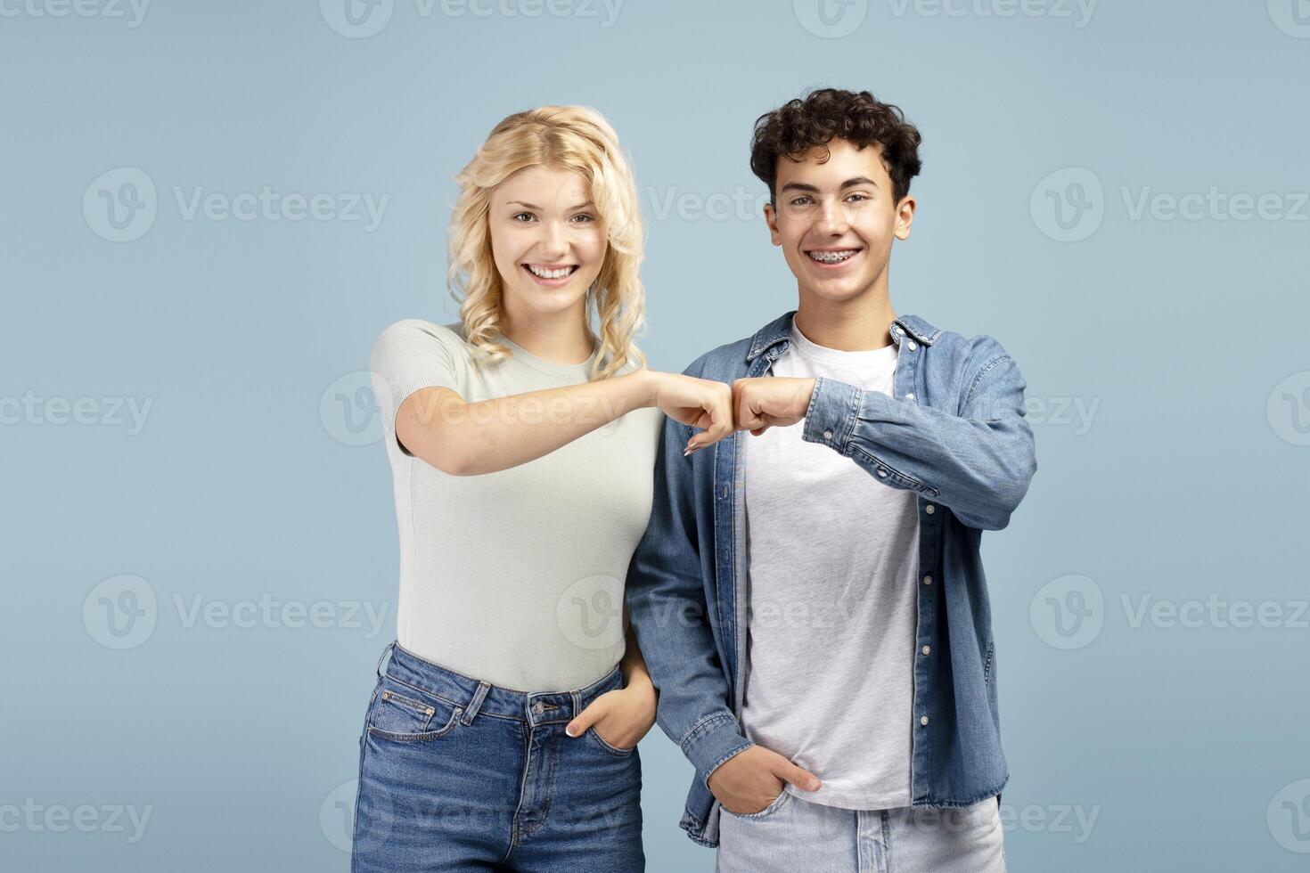 Happy, smiling teenagers, young boy and girl giving fist bump each other, looking at camera photo
