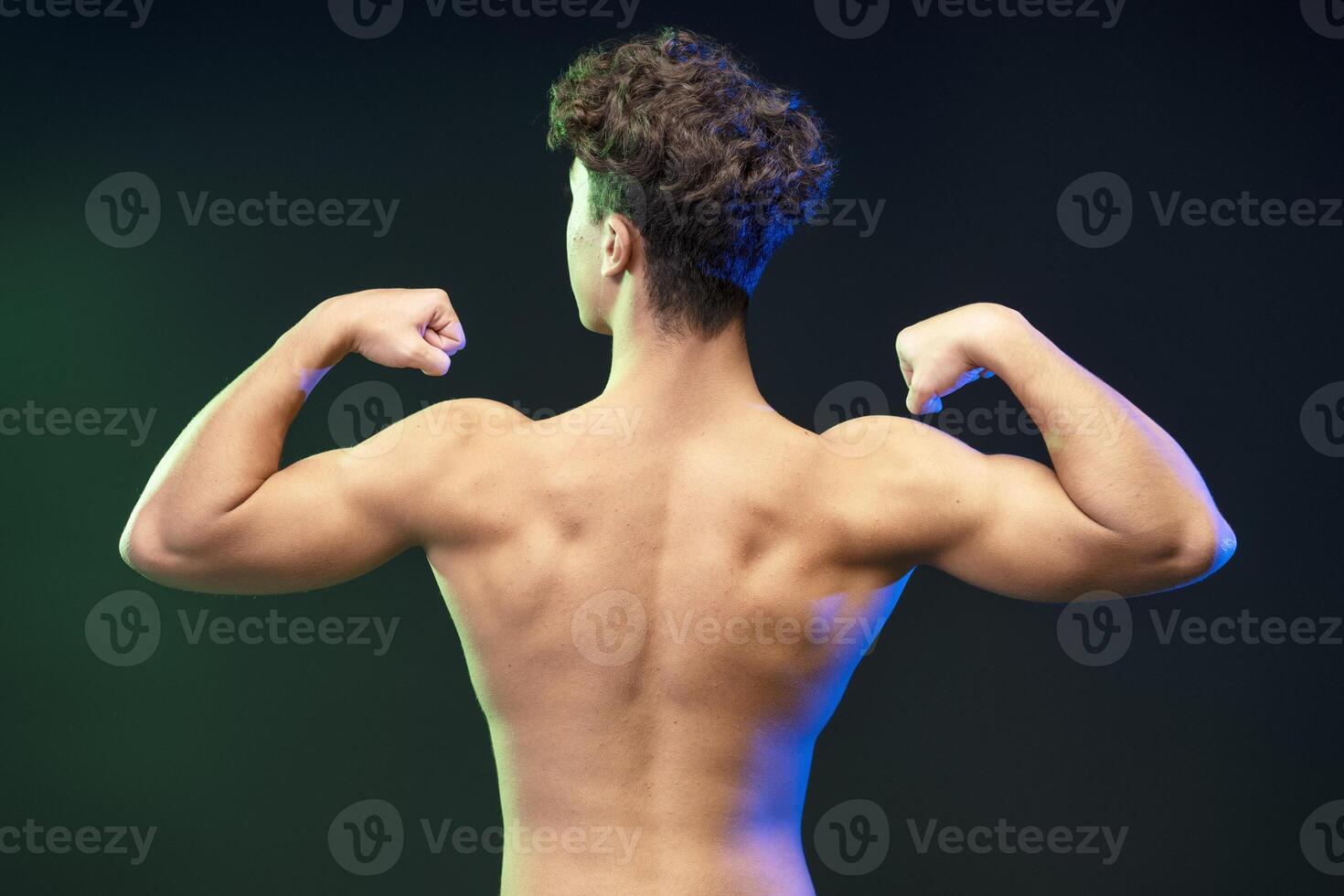 Back view, portrait of strong young boy, teenager showing muscular body isolated on black background photo