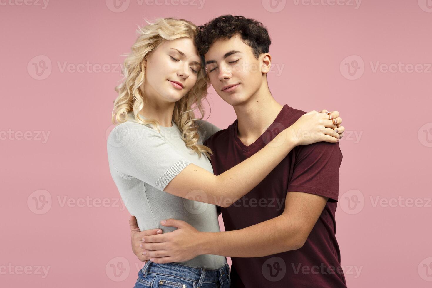 Beautiful, attractive couple hugging together with closed eyes standing isolated on pink background photo