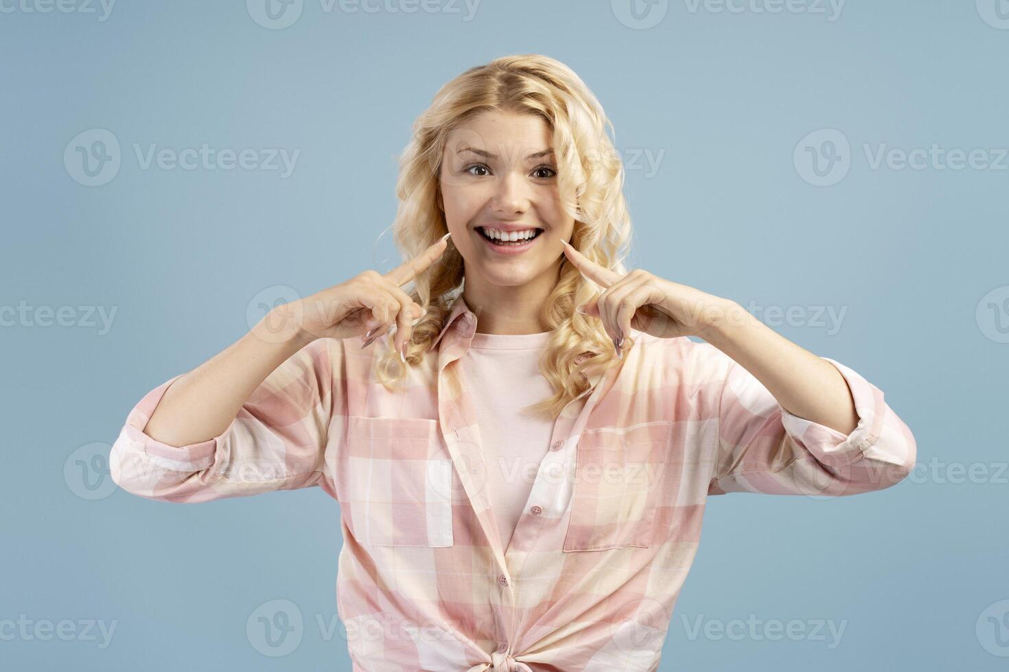 Smiling, beautiful woman wearing casual clothes looking at camera, pointing finger on teeth photo