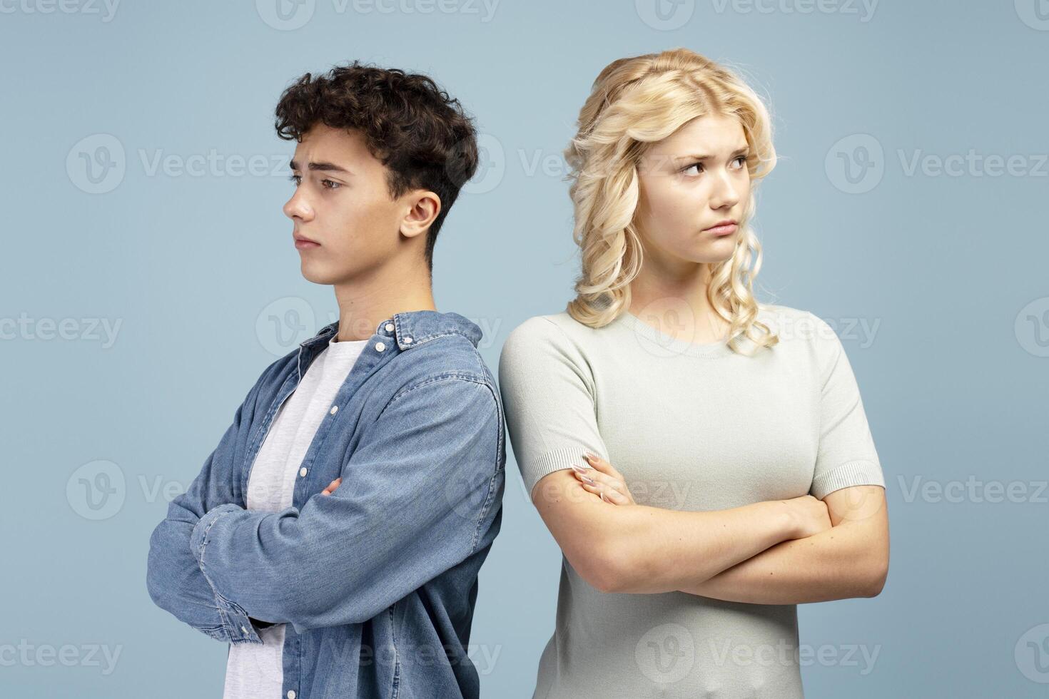 Sad quarreling couple, young guy and girl with crossed arms standing looking away photo