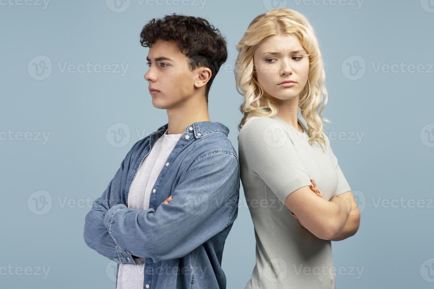 Unhappy quarreling couple, young guy and girl with crossed arms standing, back to back, looking away photo