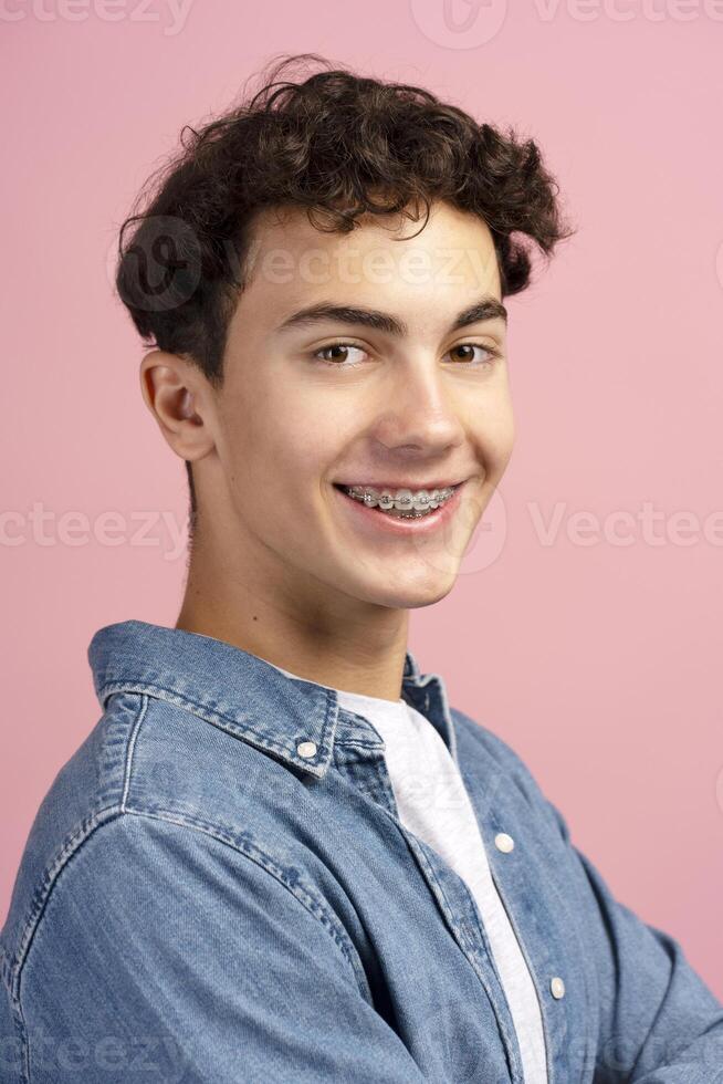 Closeup, happy, attractive teenager, boy with braces wearing casual clothes on pink background photo