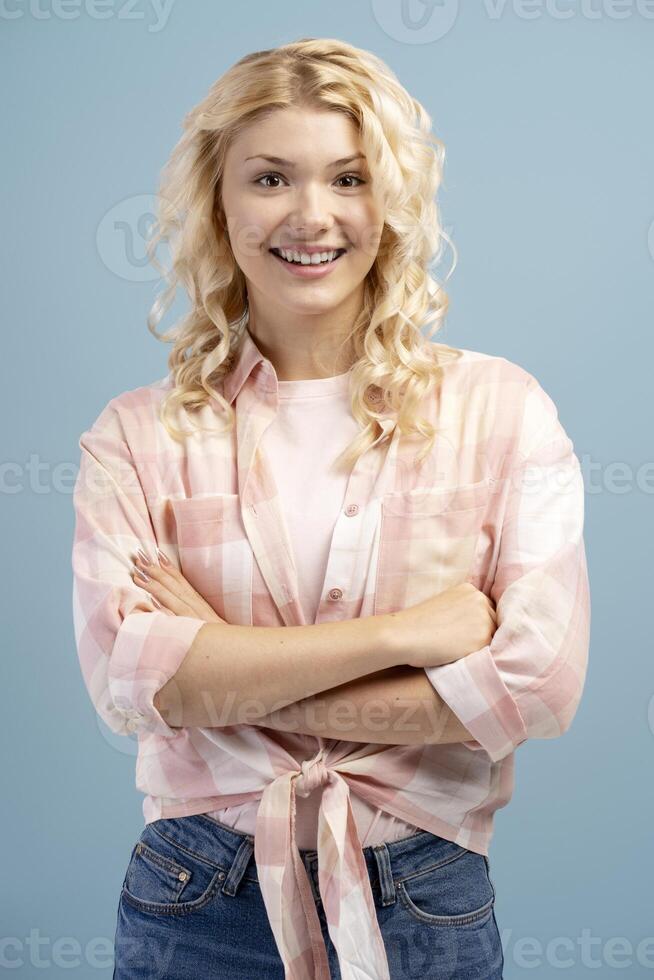 Closeup, smiling, cheerful blonde teenager with crossed arms posing isolated on blue background photo