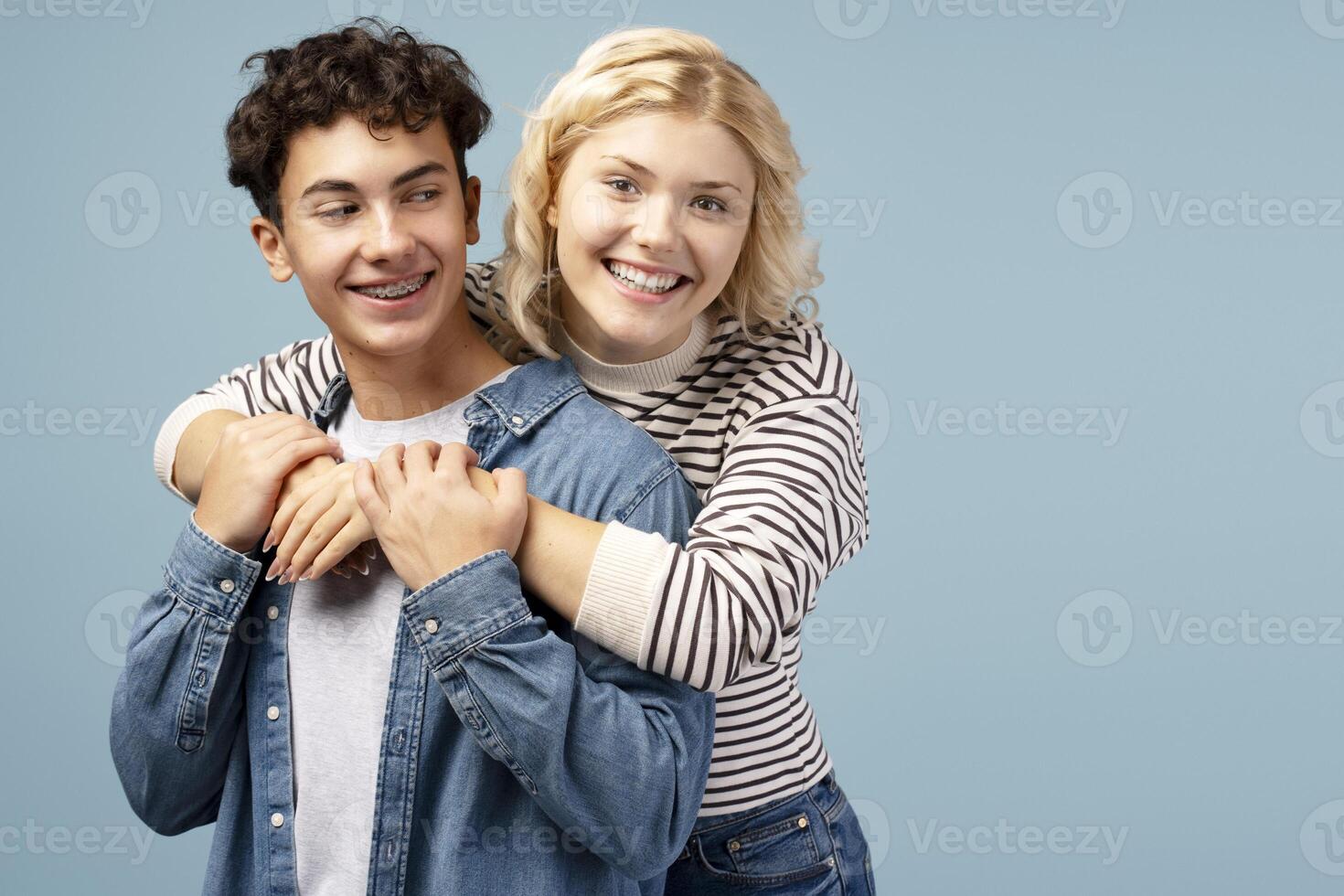 Portrait of handsome boy and beautiful girl embracing together, looking at camera on blue background photo