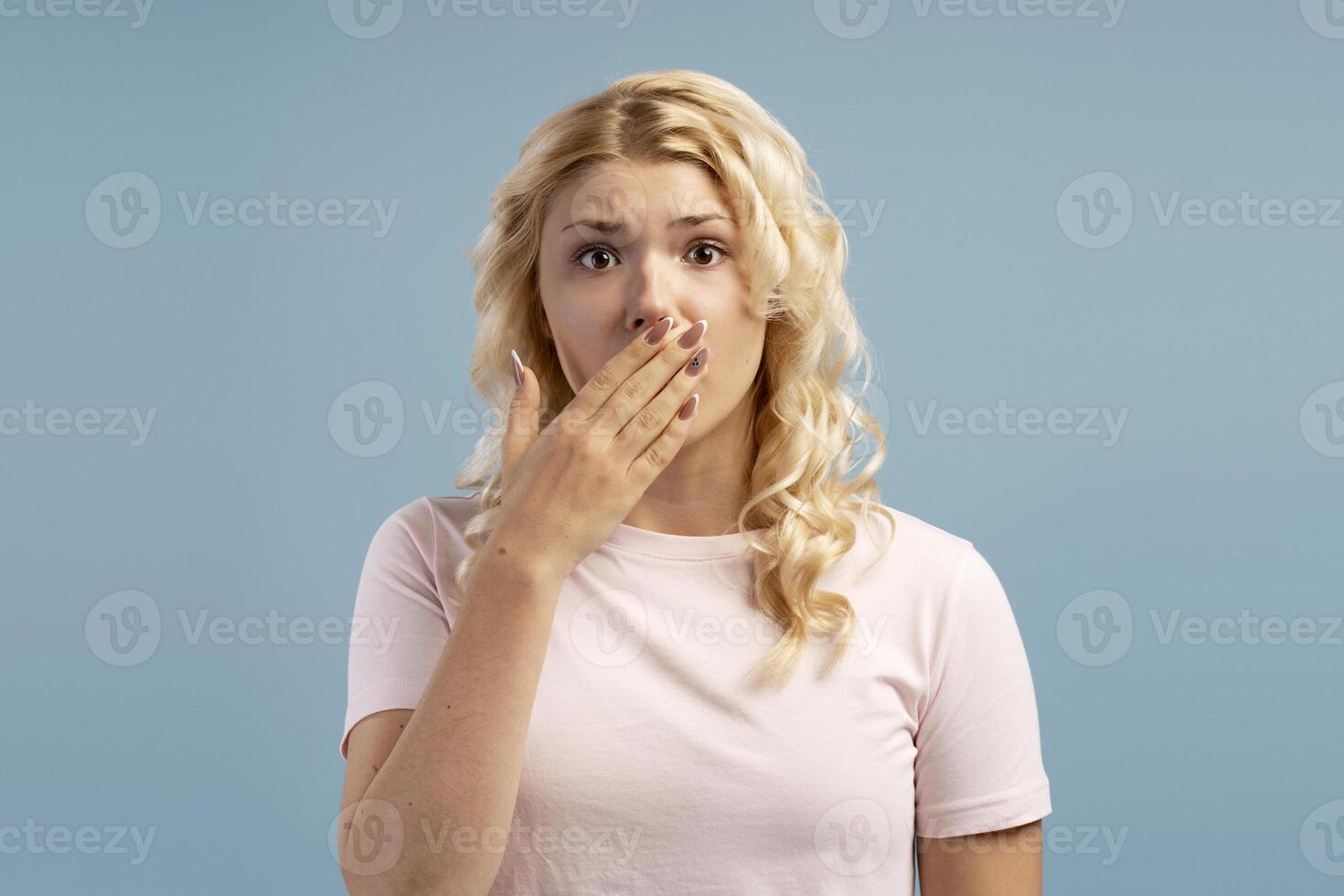 Portrait of sad blonde teenager, beautiful girl covering mouth, looking at camera, secret concept photo