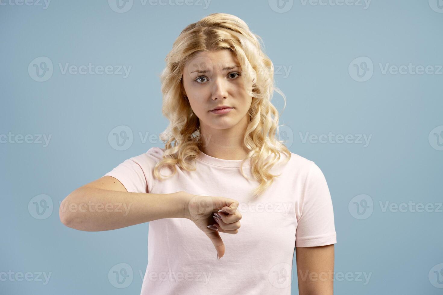Unhappy, teenager, girl showing thumb down, looking at camera, posing isolated on blue background photo