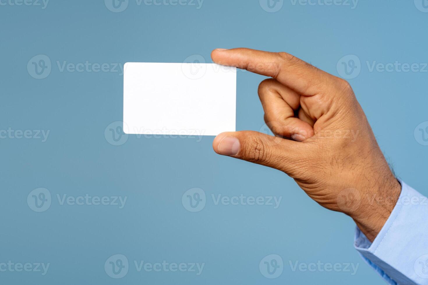 Businessman holding empty white business card, selective focus on hand isolated on blue background photo