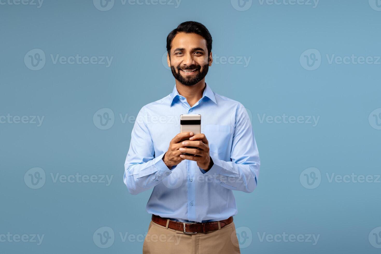 Portrait of smiling, happy bearded middle aged Indian man holding mobile phone, using mobile app photo
