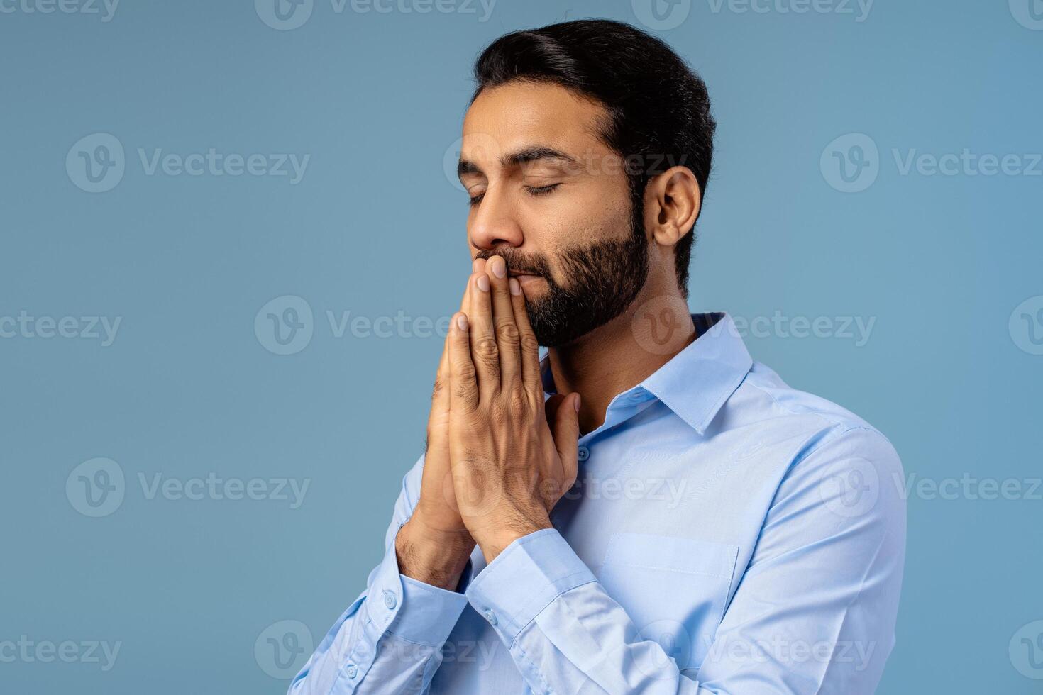 Portrait of handsome, bearded, middle aged Indian man holding hands praying with closed eyes photo