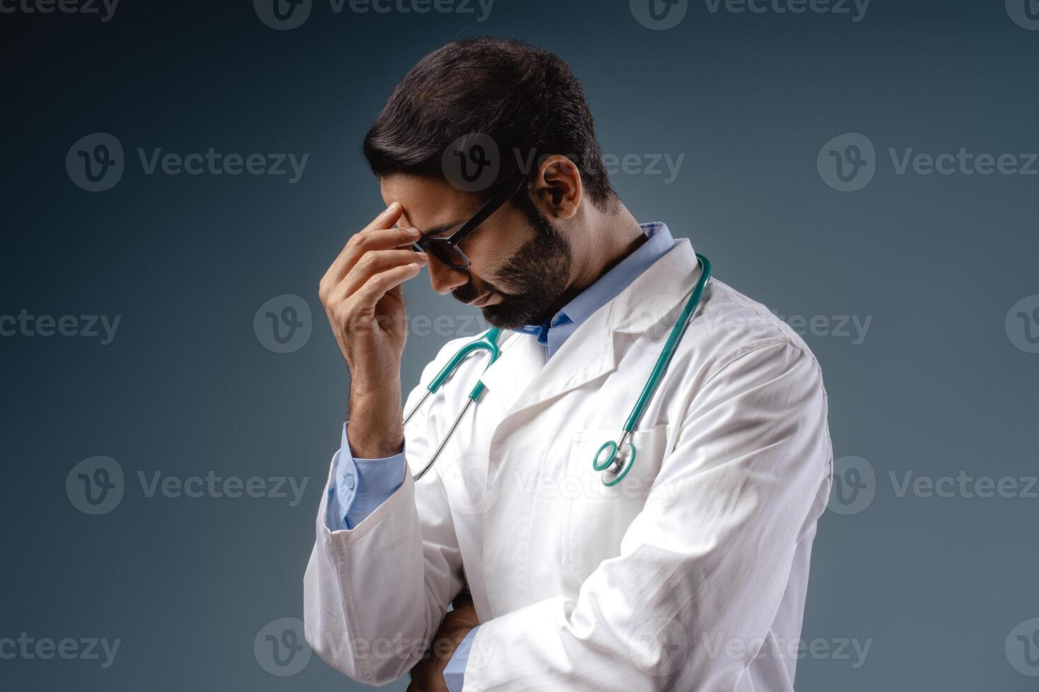 Sad, unhappy pensive Indian man, doctor wearing white coat, stylish eyeglasses, touching head photo