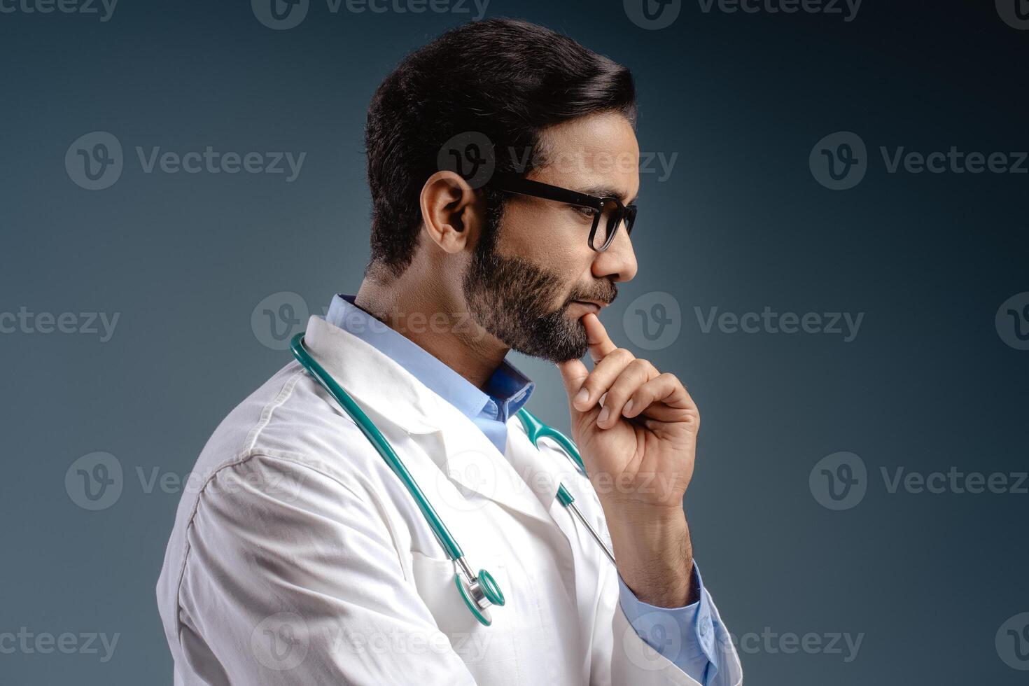 Serious, pensive Indian man, doctor wearing white coat, stethoscope, stylish eyeglasses thinking photo