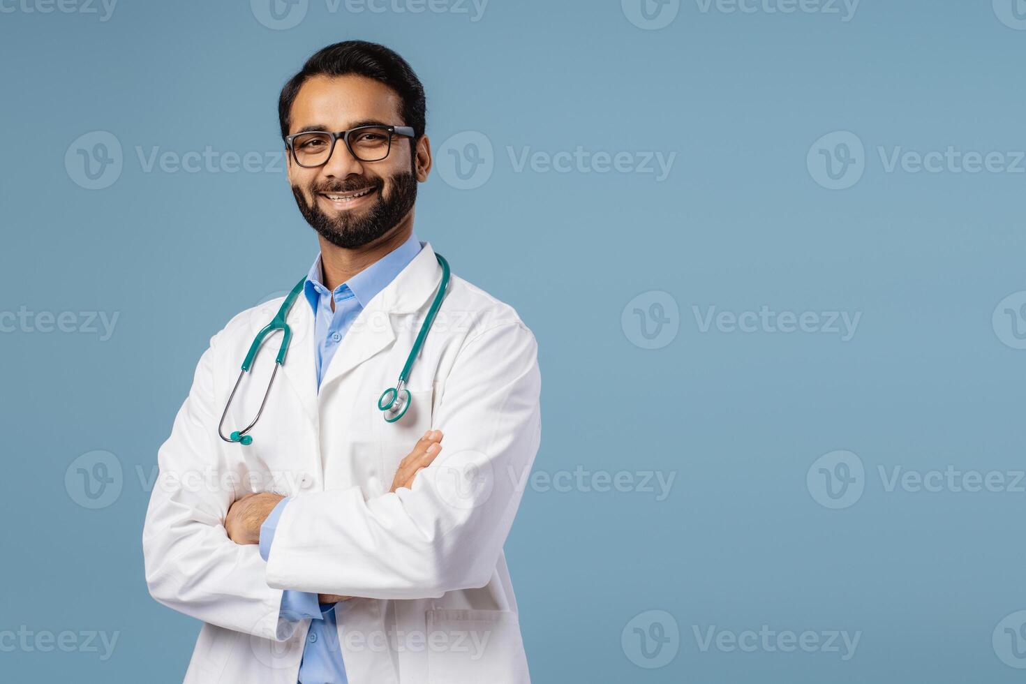 Smiling, Indian doctor wearing white coat and stethoscope and stylish eyeglasses with crossed arms photo