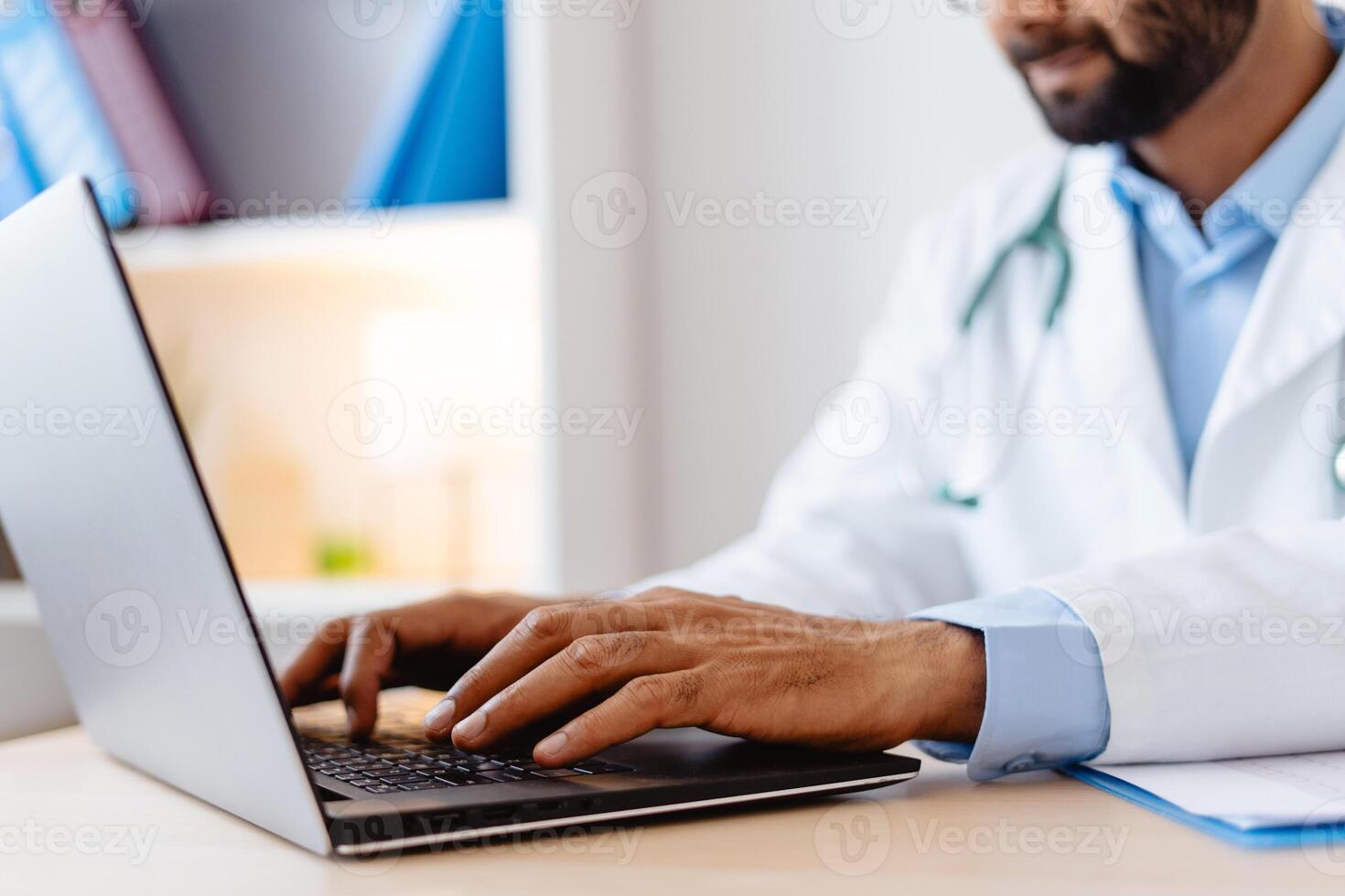 Closeup, Indian doctor in white coat, typing on keyboard, using laptop, selective focus on hands photo