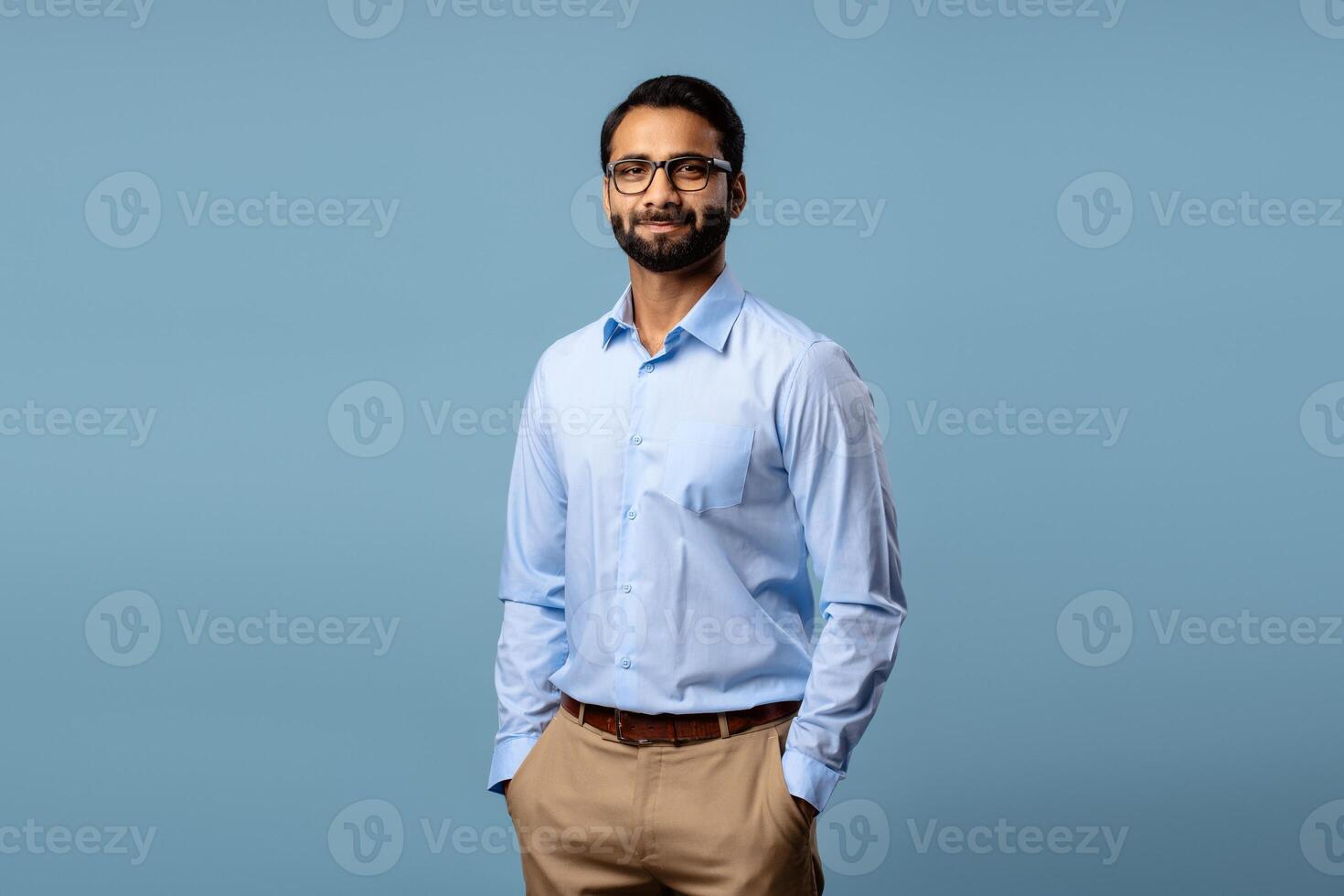 Portrait of confident Indian businessman wearing eyeglasses, hands in pockets, looking at camera photo