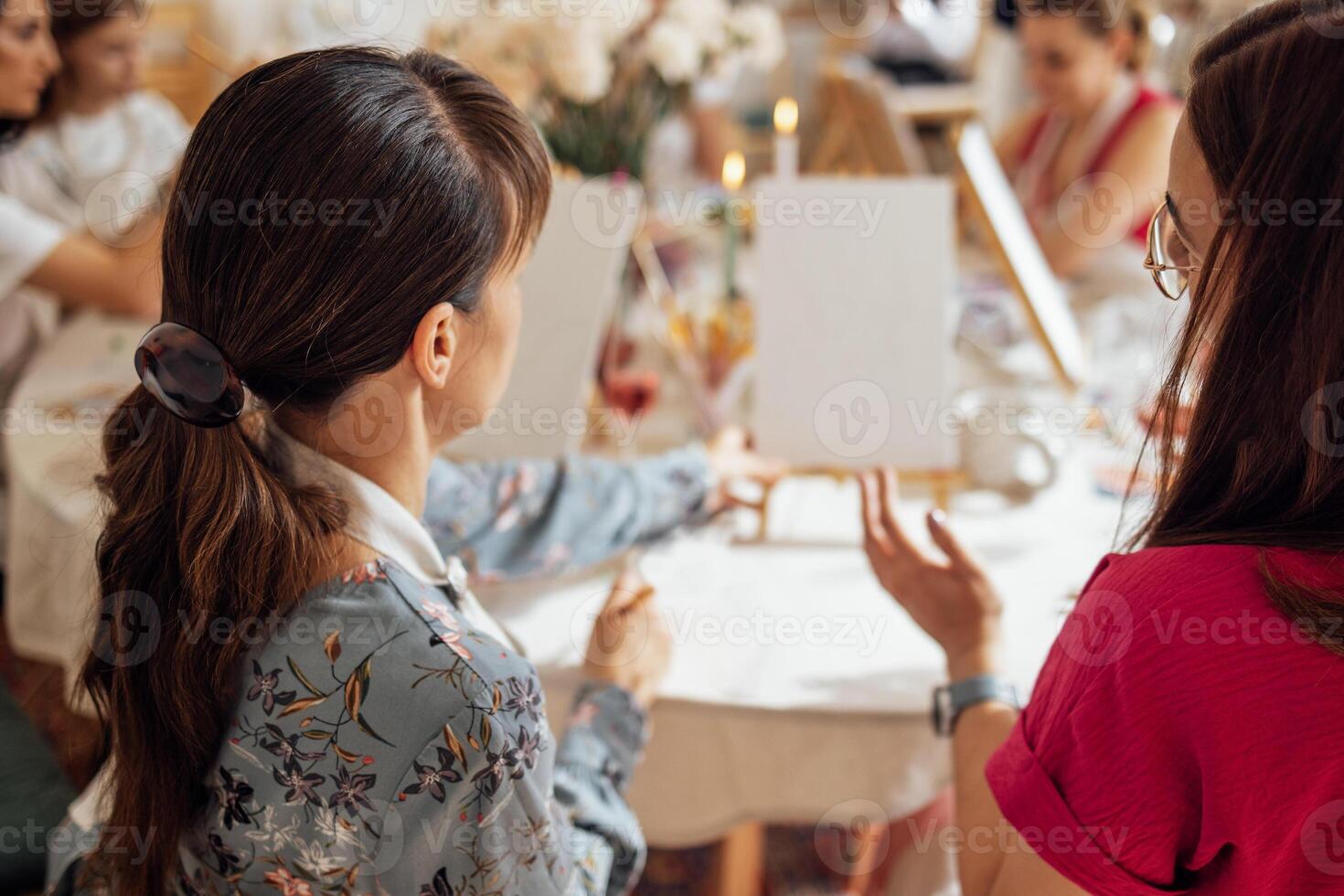 Close-up of young women in casual clothes at a painting workshop. Friends at a table with easels and blank canvases. The view from the back. photo