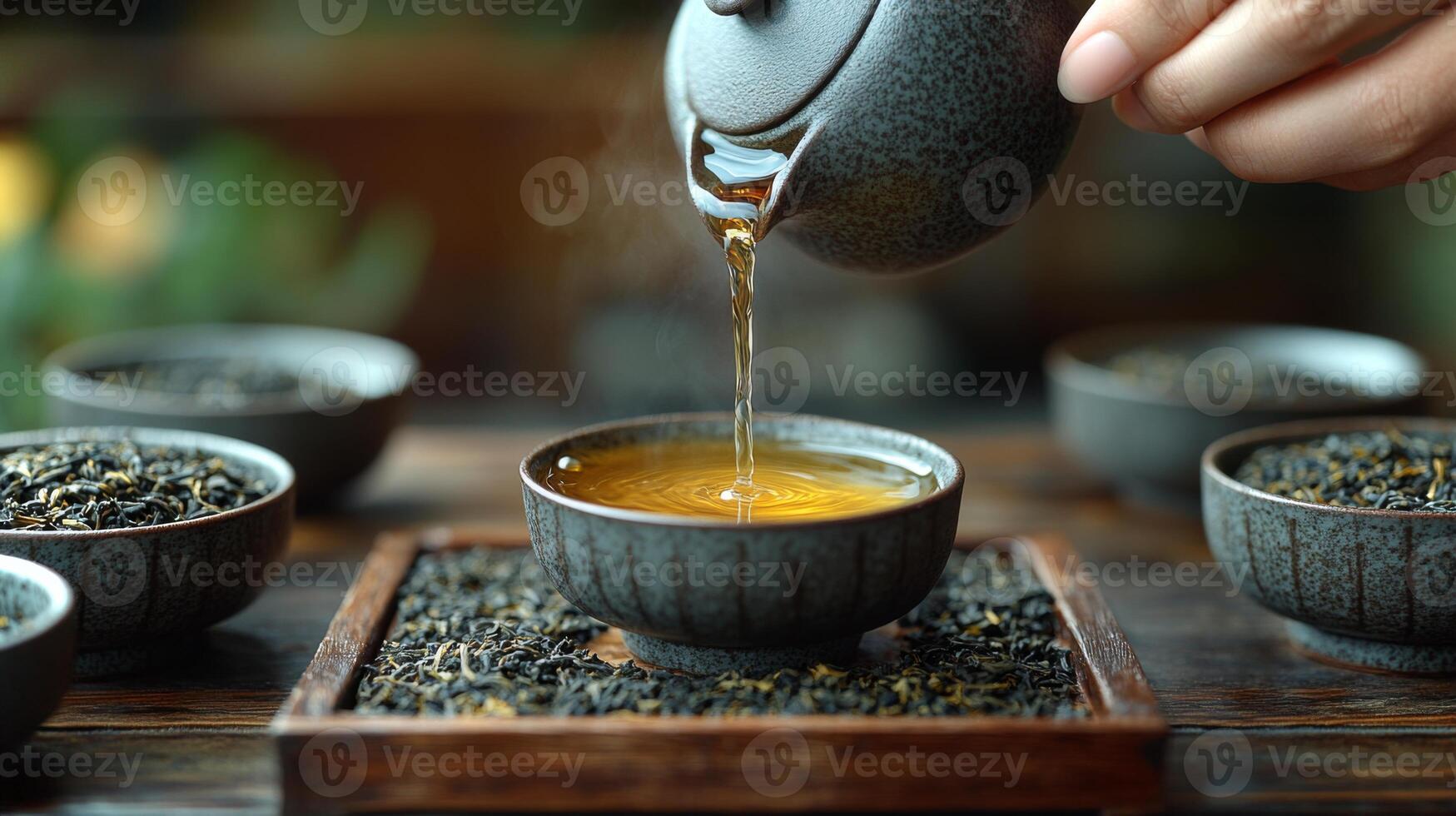 A hand gently pours warm tea from a teapot into a small cup surrounded by various types of loose leaf tea. The tranquil setting highlights an appreciation for the tea culture. photo