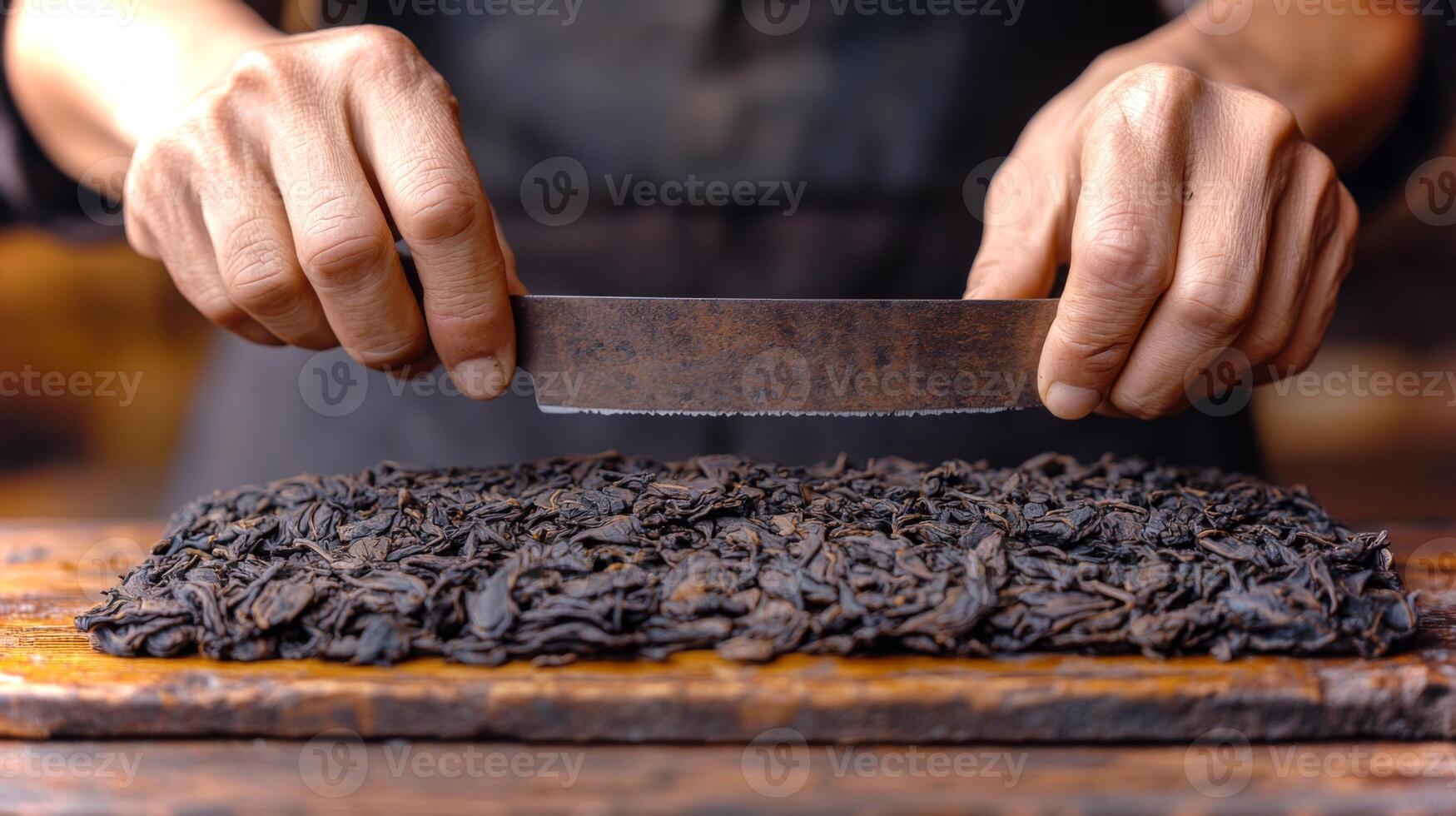 Skilled hands maneuver a sharp knife to slice through a dense block of aged tea leaves, revealing their rich texture under warm afternoon light in a workshop setting. photo