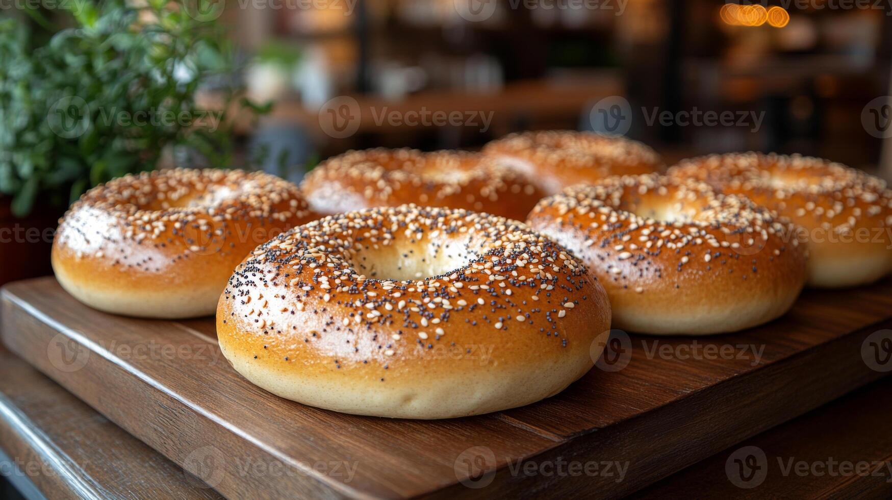 A selection of freshly baked bagels garnished with sesame and poppy seeds is displayed on a wooden board within a warm, inviting cafe setting. The cozy ambience adds to the appeal of the food. photo