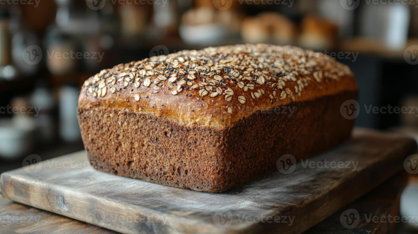 A freshly baked loaf of oat bread featuring a golden crust and sprinkled with oats rests on a wooden cutting board. The warm kitchen ambiance adds a welcoming feel to the setting. photo