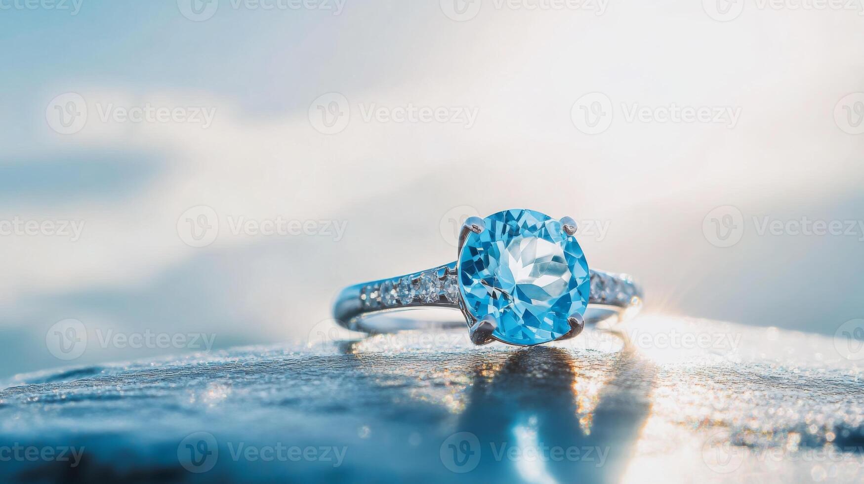A stunning blue gemstone ring rests on a smooth surface, reflecting sunlight. The intricate band sparkles, creating an enchanting effect against a soft, blurred background. photo